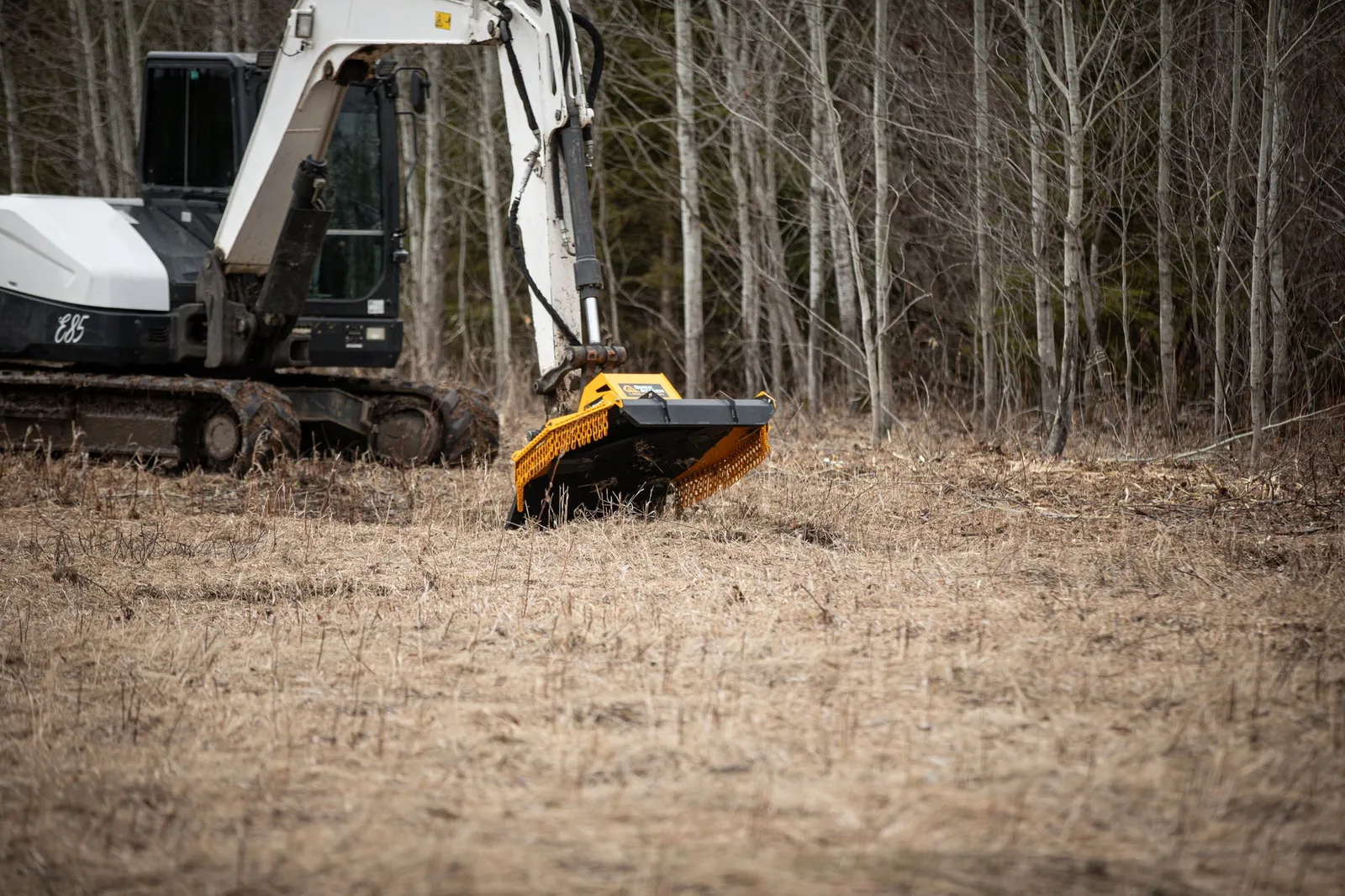 Excavator with a mulching head working on overgrown ground
