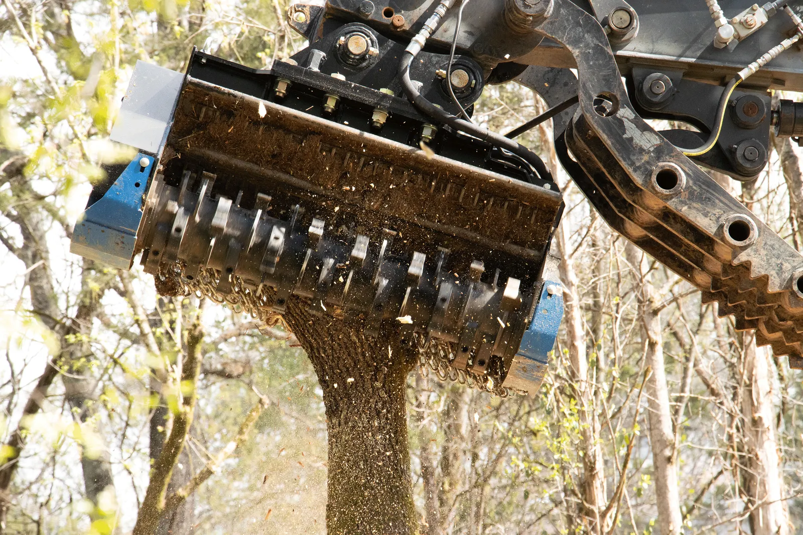 Close view of a forestry mulcher head grinding brush, with a stream of fresh wood chips pouring out